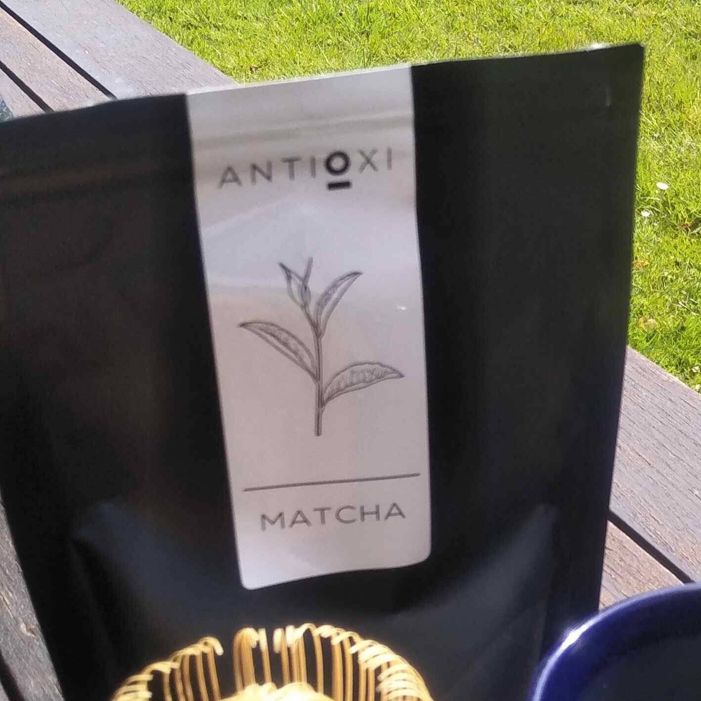 Antioxi Matcha pouch placed outdoors on a wooden surface, emphasizing the product's sleek black packaging and clear labeling with an illustration of a tea leaf.