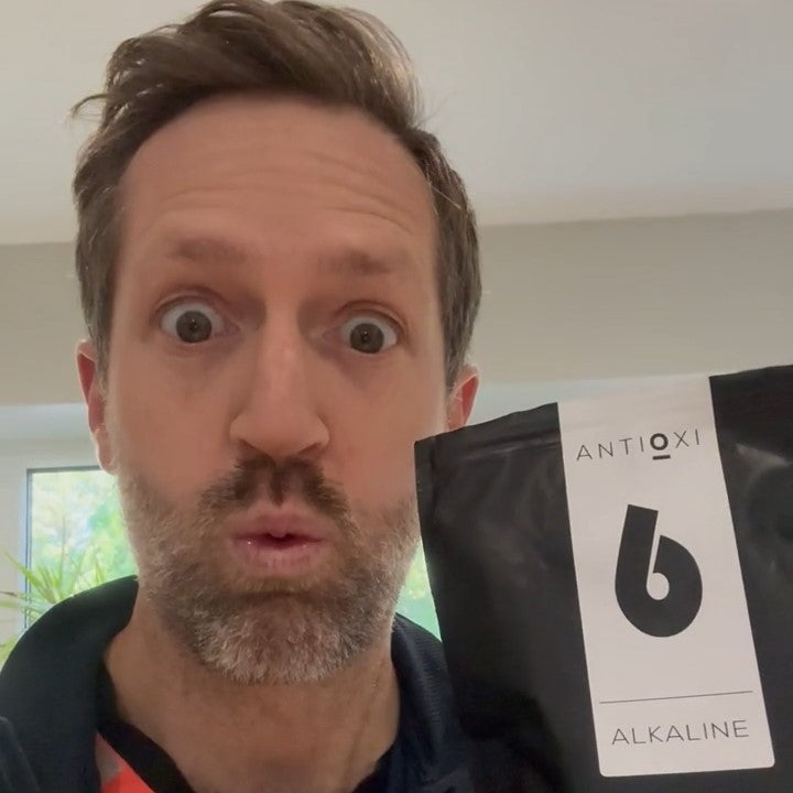  Man holding a package of Antioxi Alkaline Greens blend with an excited expression.