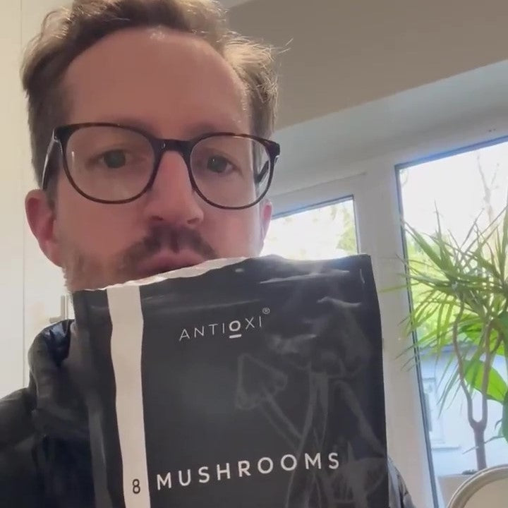 A person holding a package of Antioxi 8 Mushroom Blend supplement.