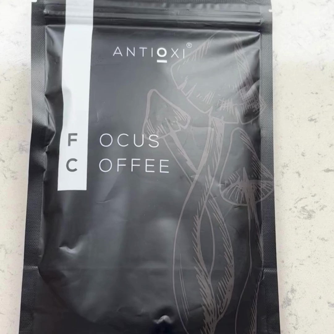 A pouch of Antioxi focus mushroom coffee placed on a white surface, showing the sleek black packaging with light gray illustrations of mushrooms.