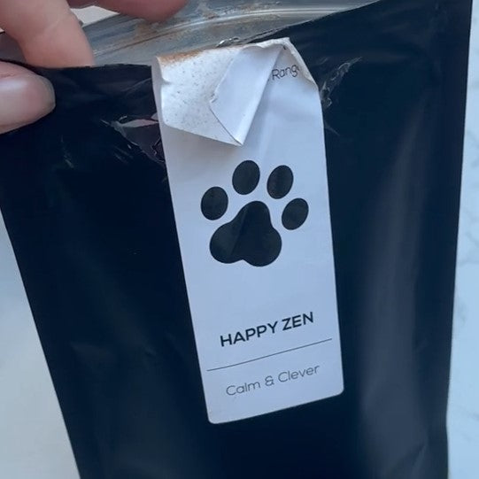 A close-up of a hand holding a pouch of Antioxi Calm & Comfort Blend mushroom supplements, showcasing the product's sleek black packaging and clear labeling with an illustration of a Paw print.