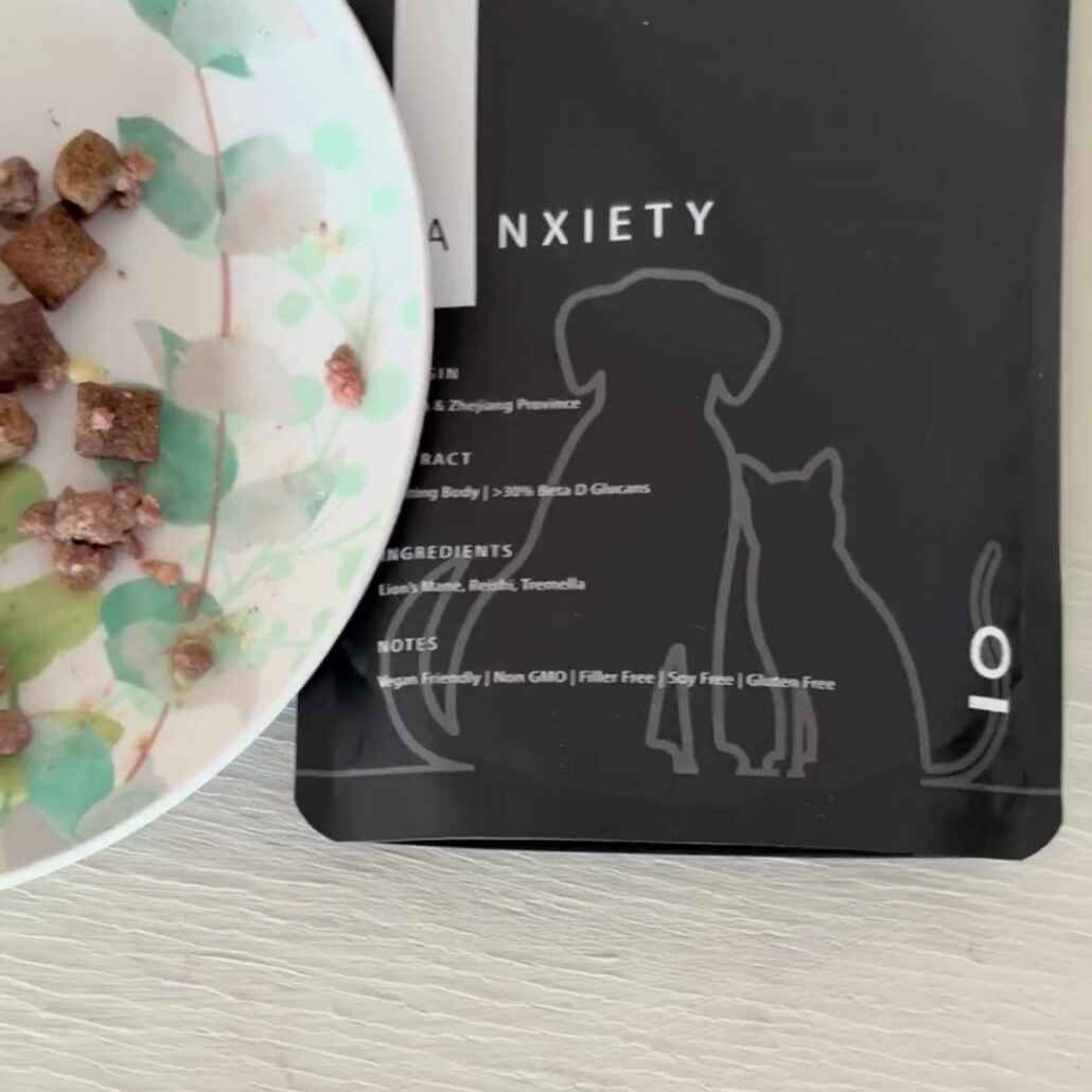 A partial view of a pet food bowl with kibble on a table, next to a black pouch of Antioxi's Calm & Comfort Blend for Pets.