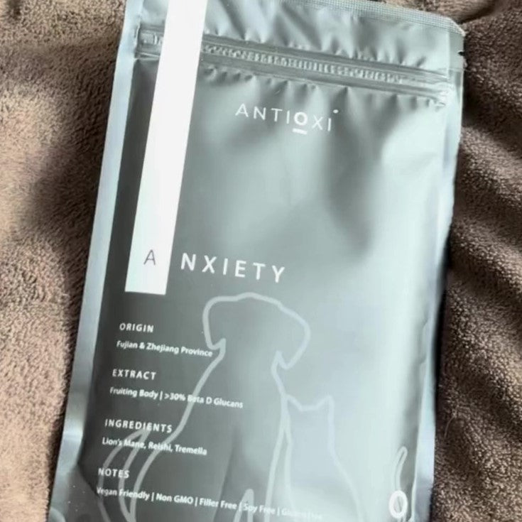 A close-up of a black pouch of Antioxi Calm & Comfort Blend for pets placed on a brown, soft surface. The black packaging reflects in the light, with clear text about its origin, extract, and extraction method.