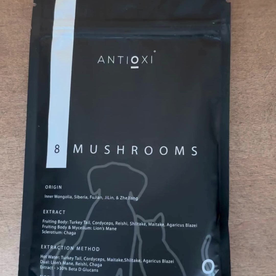 A close-up of a black pouch of Antioxi 8 Mushrooms Blend mushroom supplements for pets placed on a brown, wooden surface. The black packaging has clear text about its origin, extract, and extraction method.