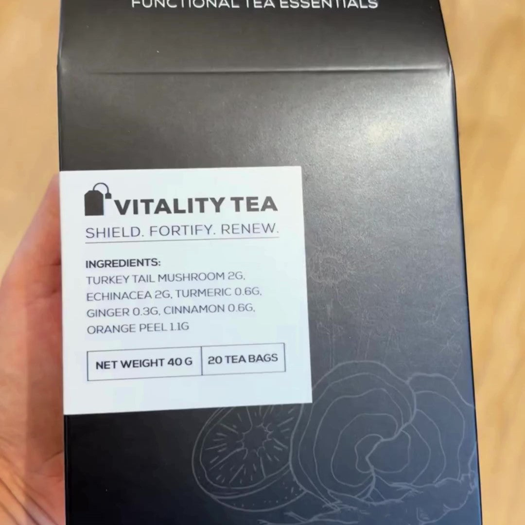 A close-up of a hand holding an Antioxi Vitality Mushroom Tea box, showcasing its ingredients such as Turkey Tail mushroom, echinacea, turmeric, ginger, cinnamon, and orange peel.