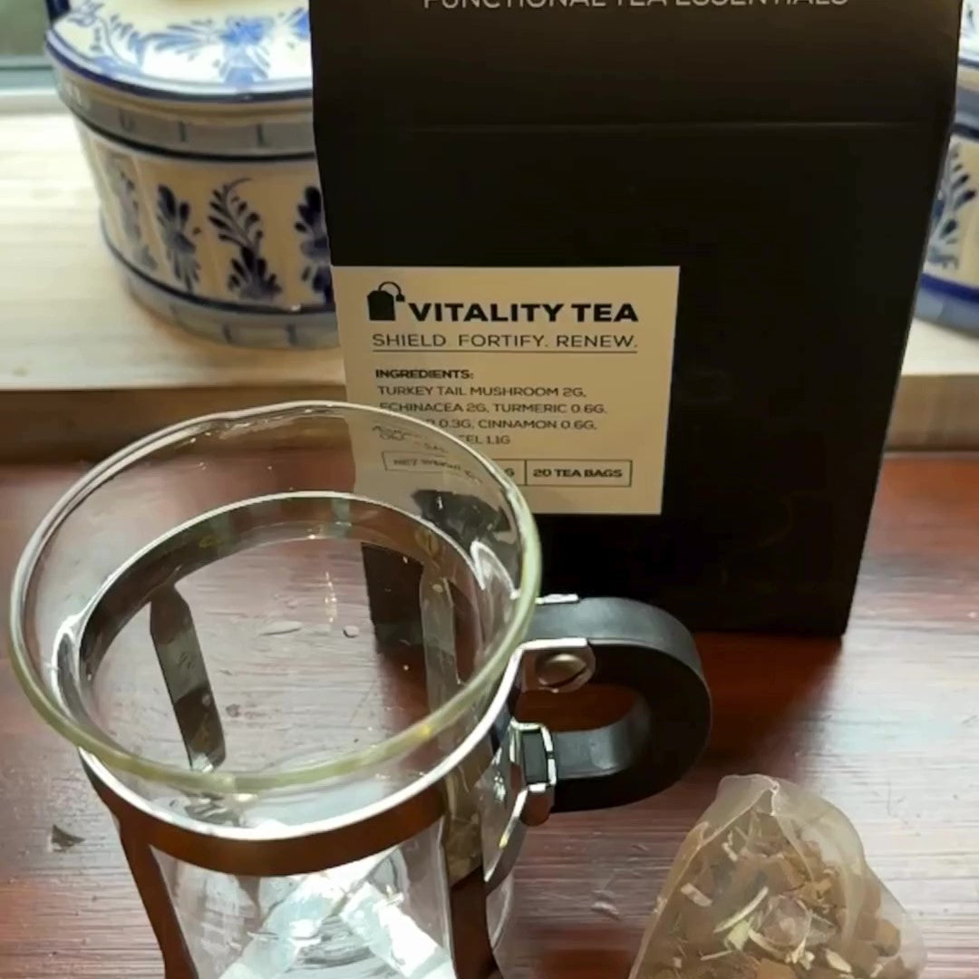 Glass tea infuser and an Antioxi Vitality Mushroom Tea tea-bag beside it, with the Antioxi Vitality Mushroom Tea box behind it.