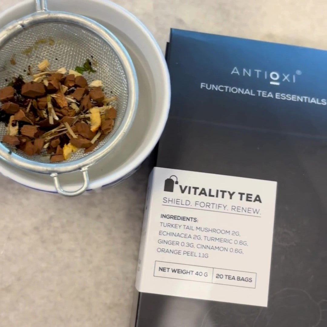 Antioxi Vitality Mushroom Tea box next to a tea strainer filled with loose leaf ingredients, on top of a white surface.