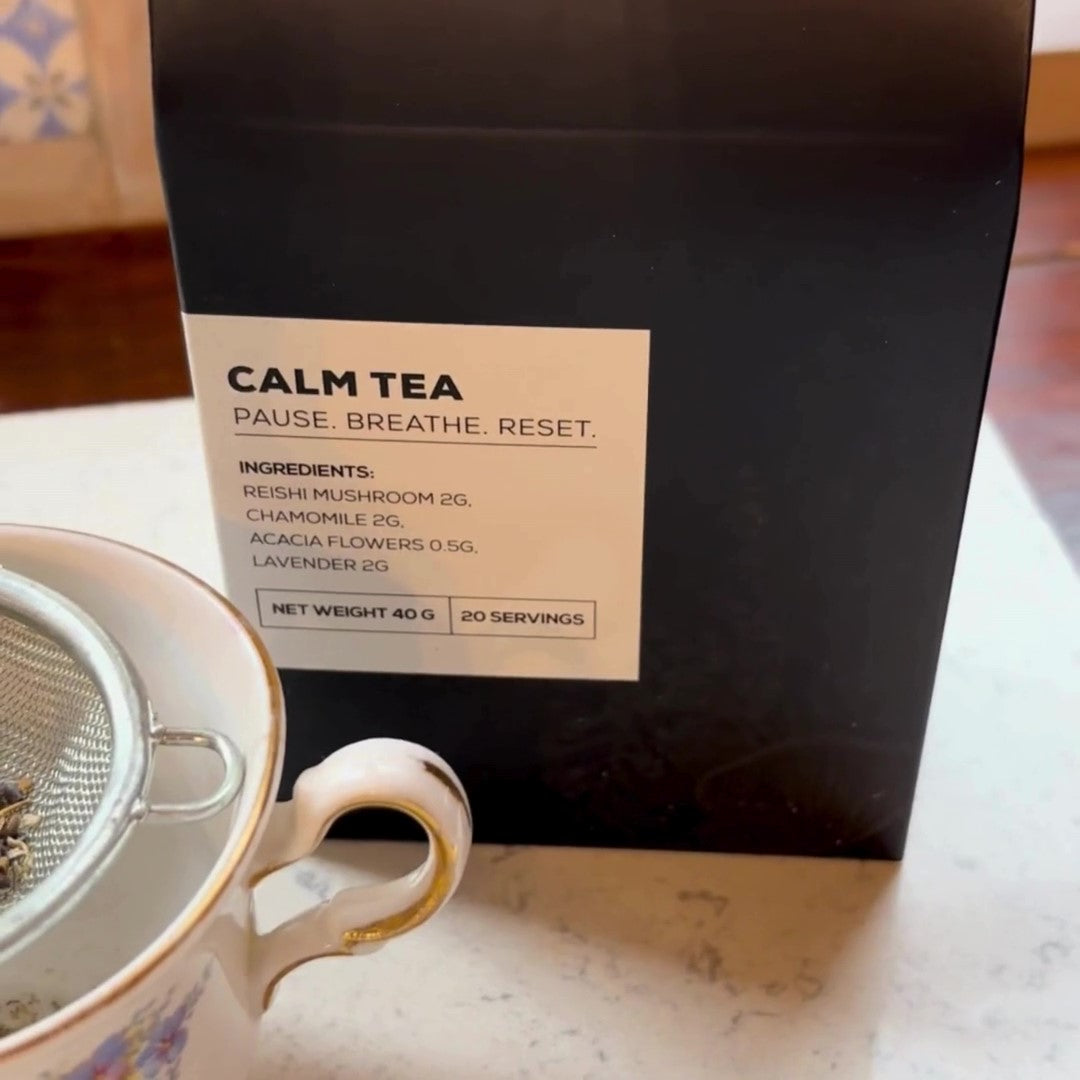 Antioxi Calm Tea packaging next to a teacup and strainer, highlighting the product's ingredients and purpose: Reishi mushroom, chamomile, acacia flowers, and lavender for a calming experience.