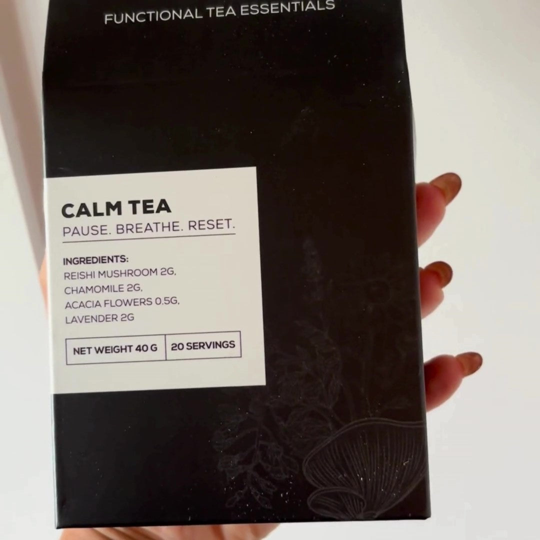 A close-up of a hand holding a black Antioxi Calm Mushroom Tea box, highlighting the product's ingredients listed on the box.