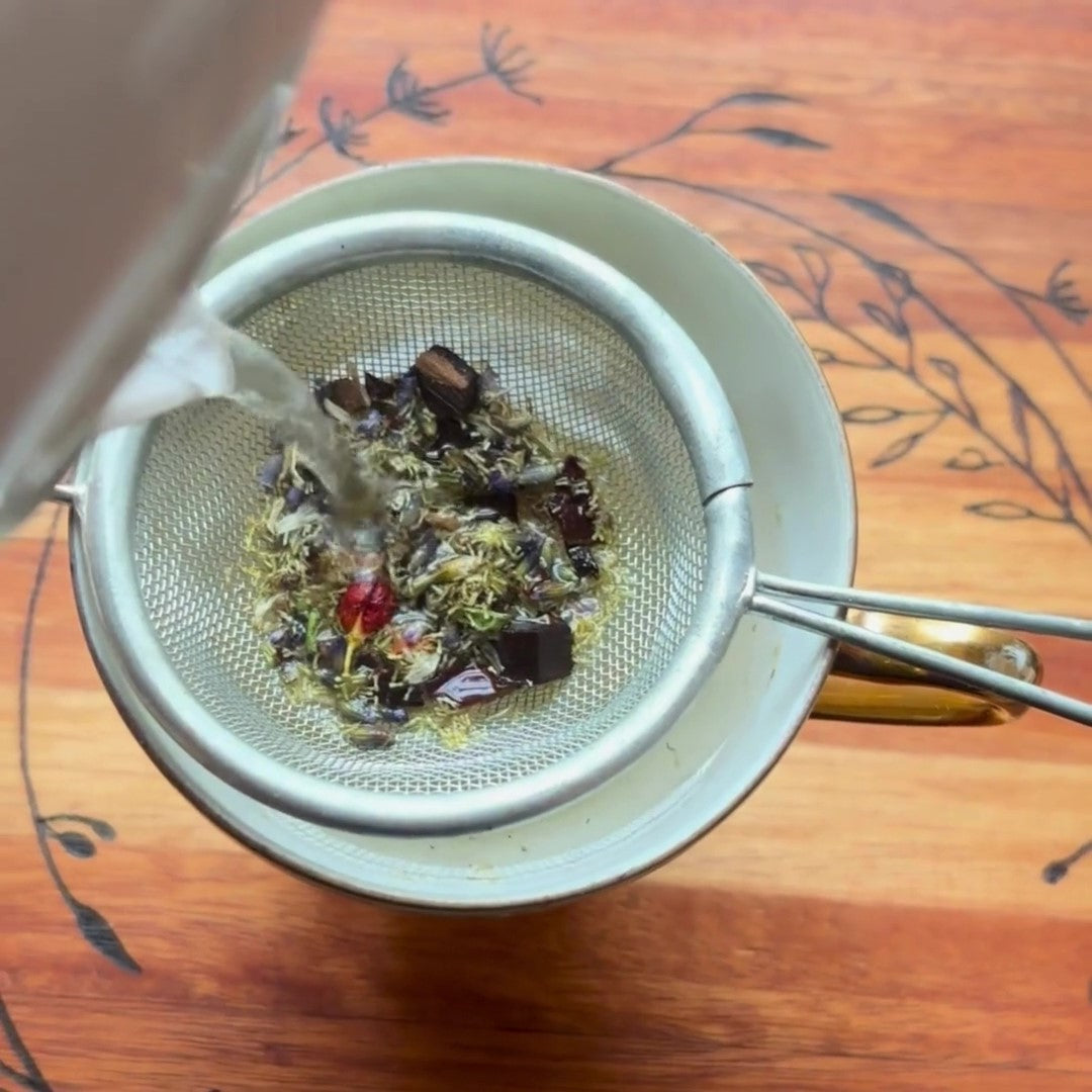 Antioxi Calm Mushroom Tea loose leaf ingredients in a tea strainer, placed over a cup, with water being poured over the ingredients.