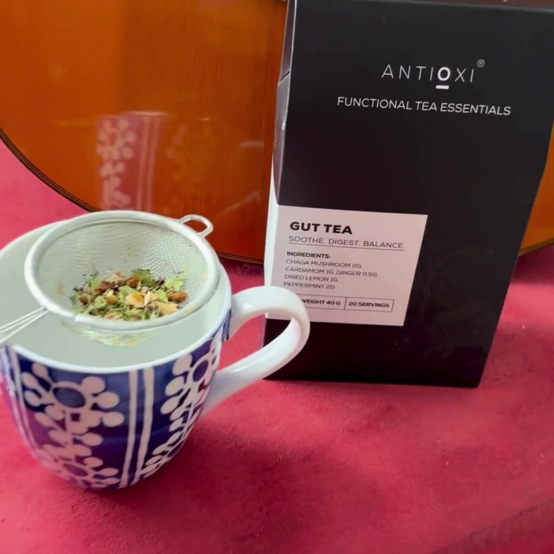 Antioxi Gut Mushroom Tea box next to a cup with tea strainer filled with loose leaf ingredients placed on top of the cup.