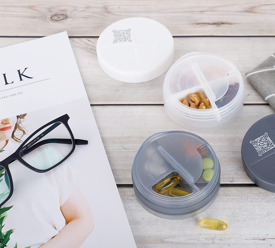 Lifestyle image of the Antioxi and Kigi pill box travel cap and lid, placed next to a magazine and glasses, highlighting its portability and convenience.